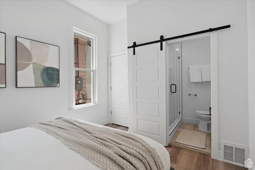 Bedroom with a barn door, wood finished floors, ensuite bath, and baseboards