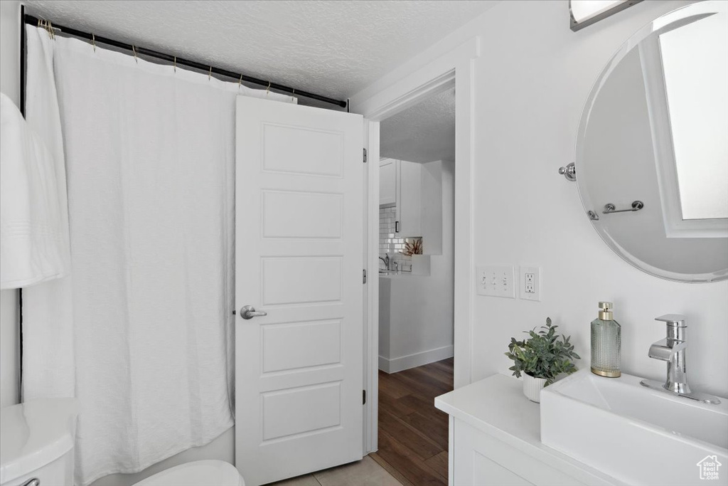 Full bathroom with toilet, a textured ceiling, vanity, wood finished floors, and curtained shower