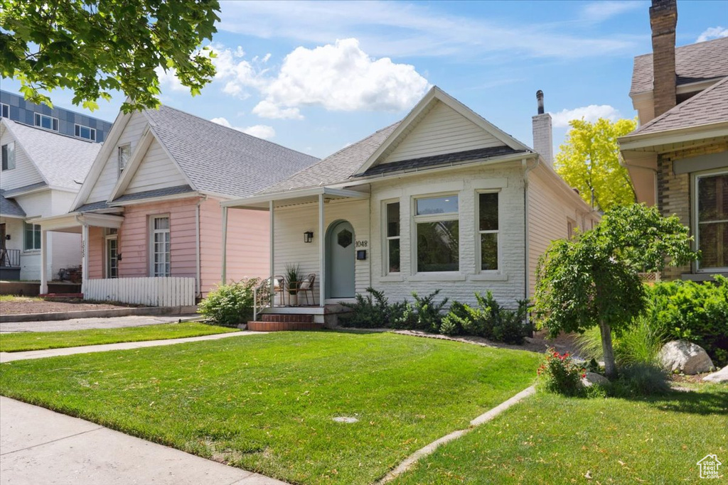 Bungalow with a front yard and a shingled roof