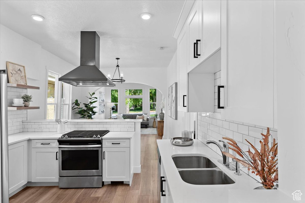 Kitchen featuring island range hood, stainless steel gas range oven, a sink, a peninsula, and light countertops