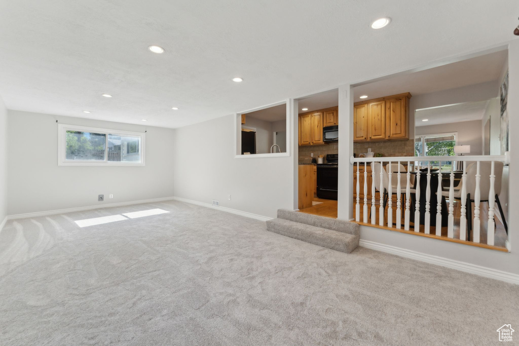 Unfurnished living room with recessed lighting, light carpet, baseboards, and plenty of natural light