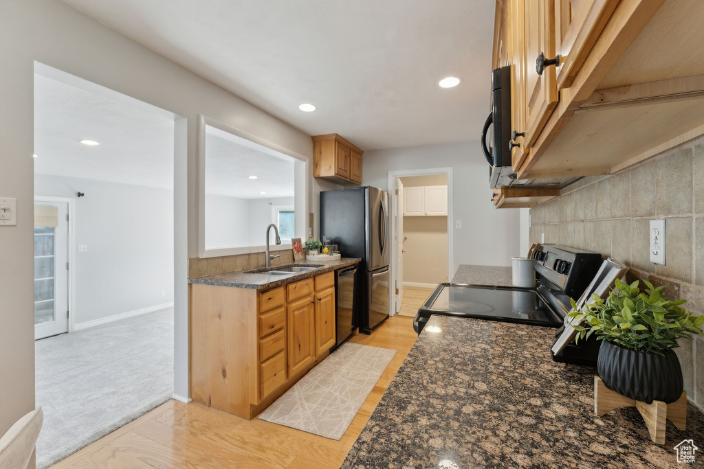 Kitchen with a sink, black appliances, recessed lighting, baseboards, and dark stone counters