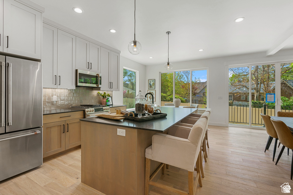 Kitchen featuring premium appliances, dark countertops, a kitchen island with sink, light wood-type flooring, and recessed lighting