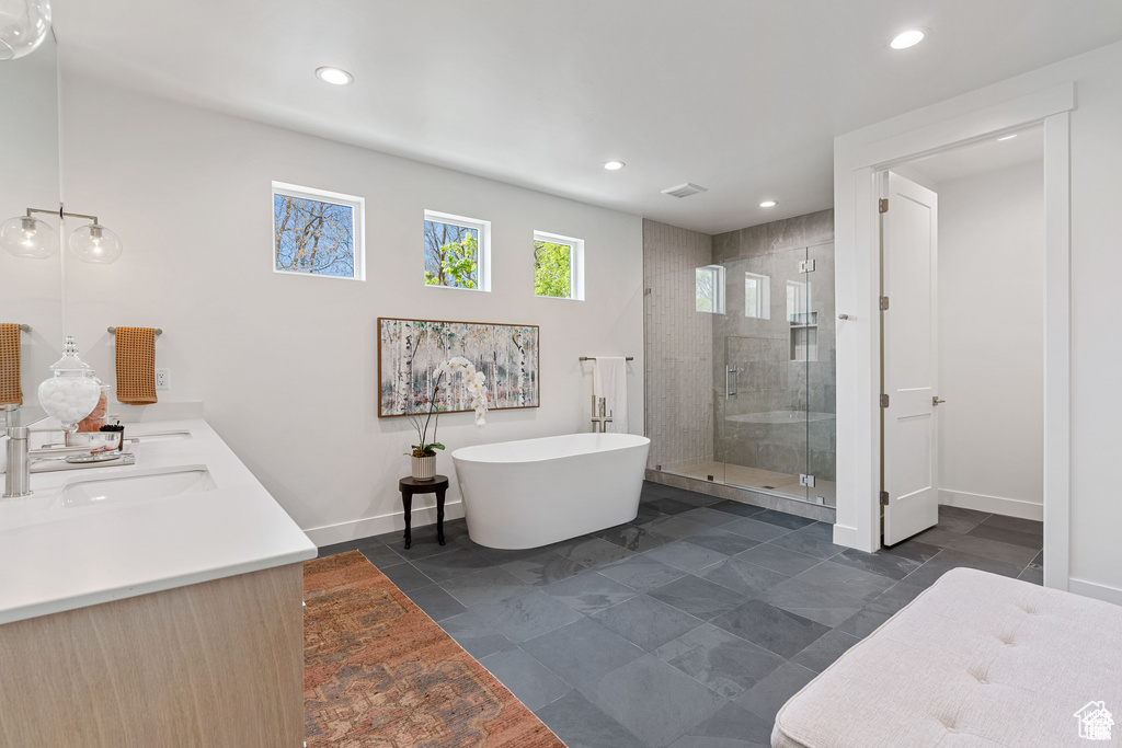 Bathroom featuring a stall shower, baseboards, a freestanding bath, double vanity, and recessed lighting