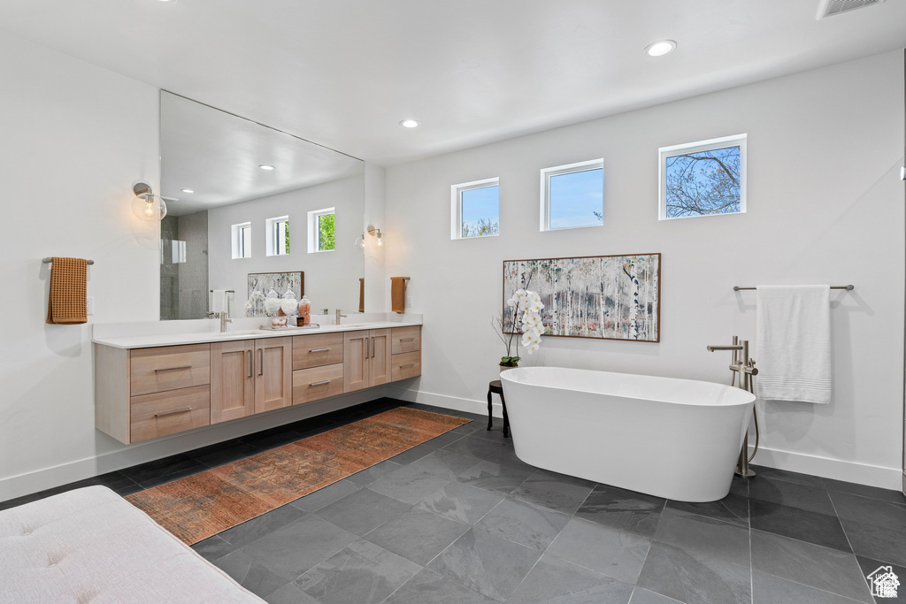 Full bath with double vanity, a soaking tub, baseboards, and recessed lighting
