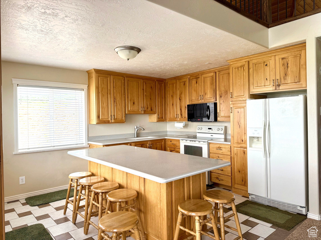 Kitchen featuring white appliances, light countertops, baseboards, a sink, and a breakfast bar