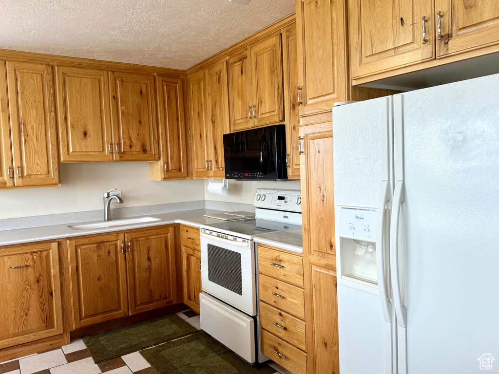 Kitchen with white appliances, a sink, a textured ceiling, light countertops, and brown cabinetry