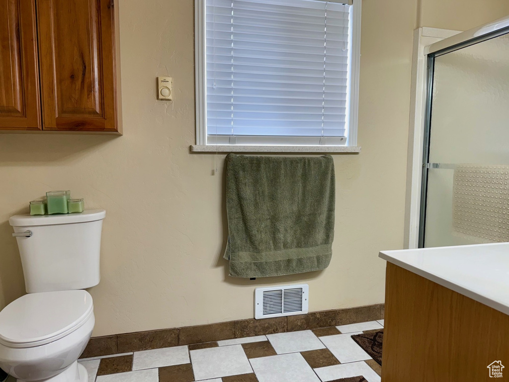 Bathroom with toilet, a shower with door, vanity, and baseboards