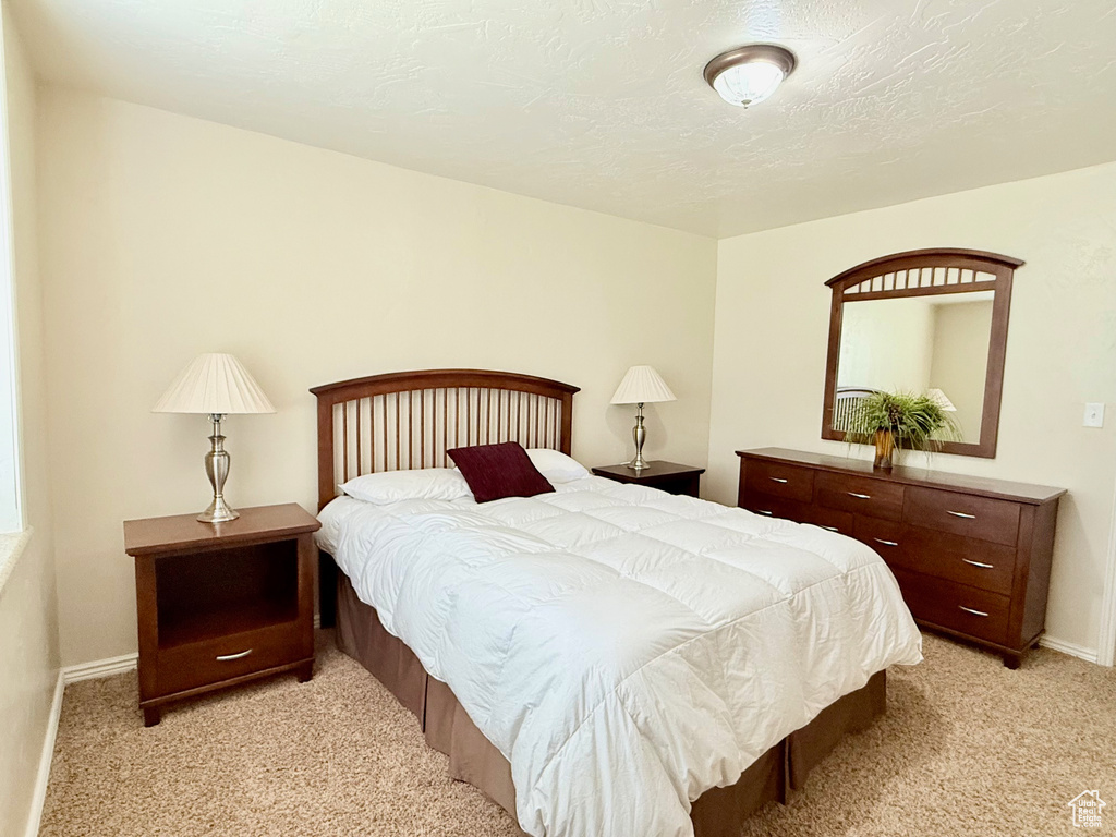 Bedroom featuring light carpet, baseboards, and a textured ceiling