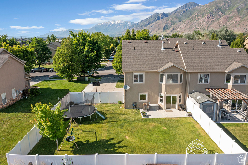 Back of house with a trampoline, a patio, stucco siding, a shingled roof, and a mountain view