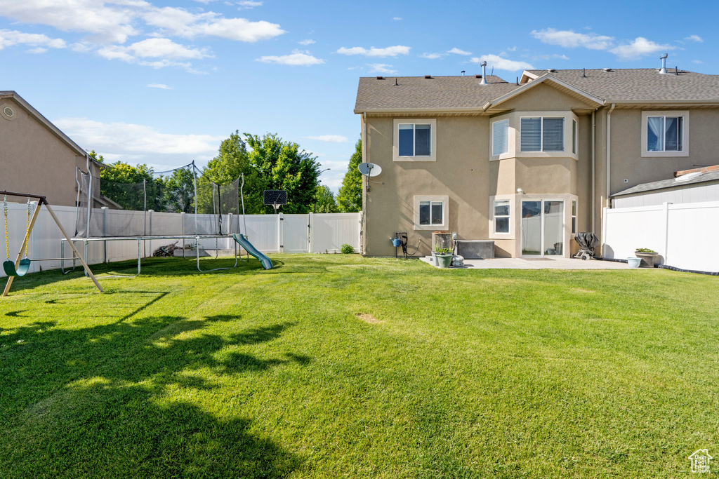 Rear view of property featuring a trampoline, stucco siding, and a patio