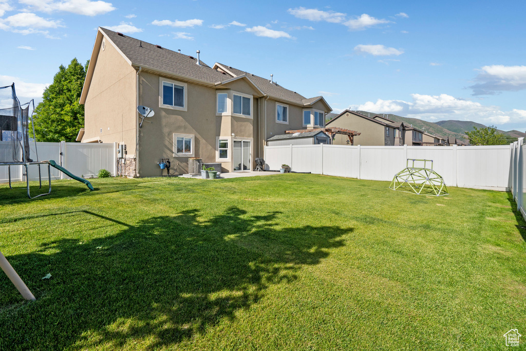 Back of property with stucco siding, a trampoline, and a patio area