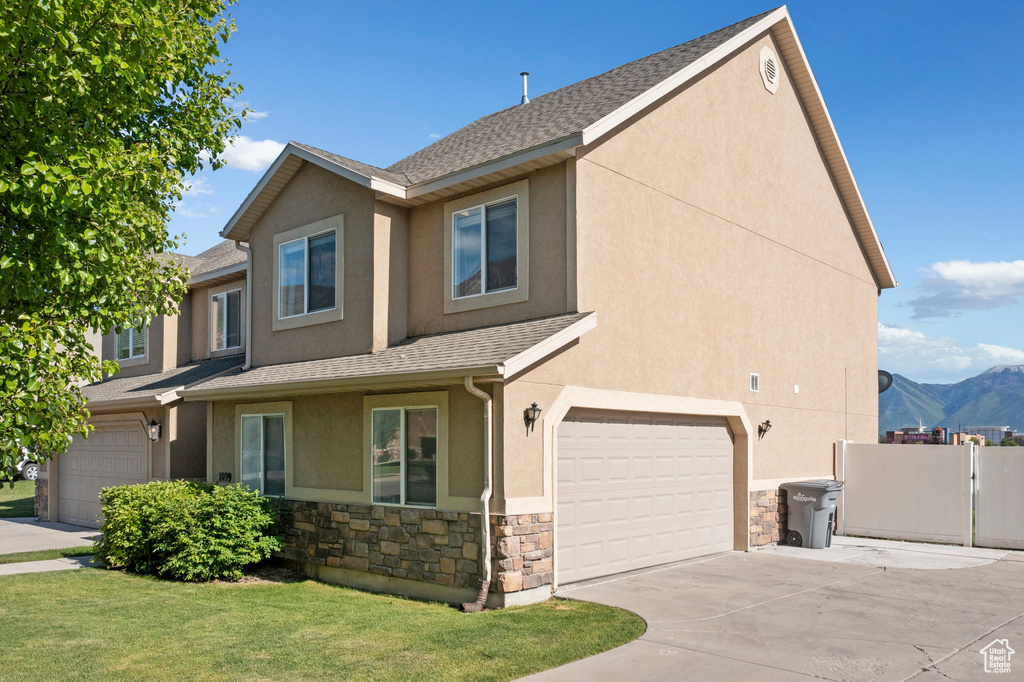 View of front facade with stucco siding, stone siding, a garage, driveway, and roof with shingles