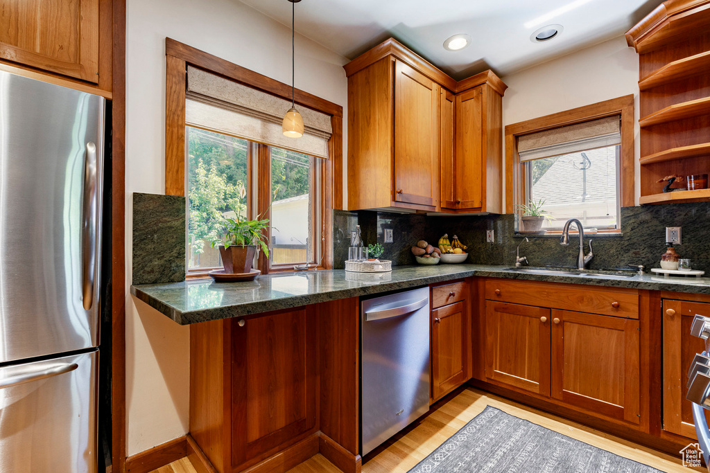 Kitchen featuring stainless steel appliances, brown cabinetry, tasteful backsplash, light wood-style flooring, and decorative light fixtures