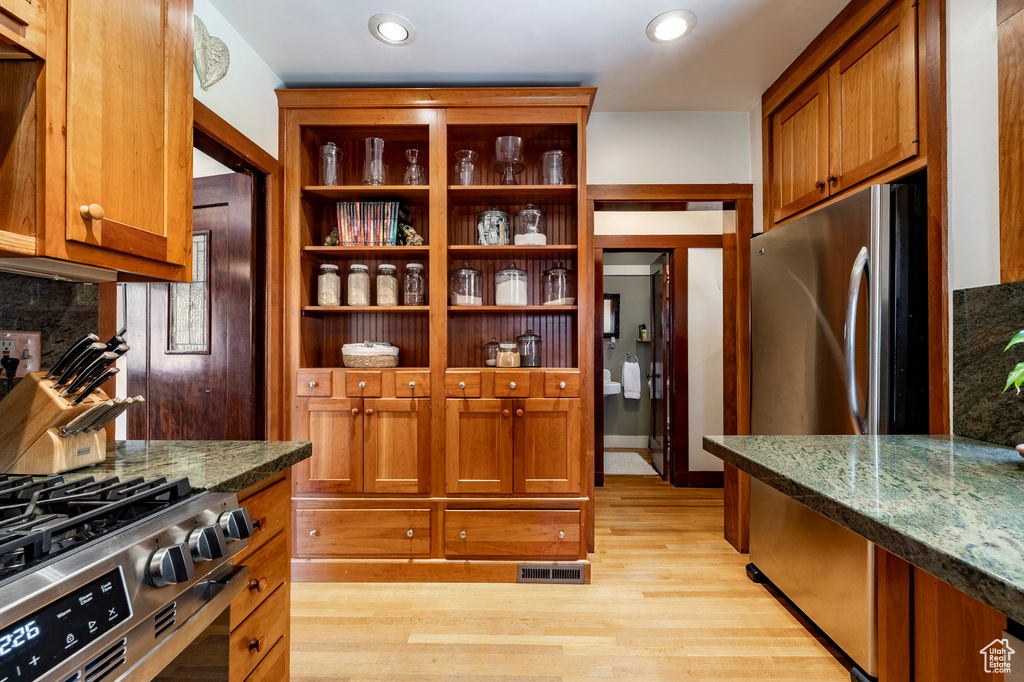 Kitchen with appliances with stainless steel finishes, open shelves, light wood-type flooring, decorative backsplash, and dark stone countertops