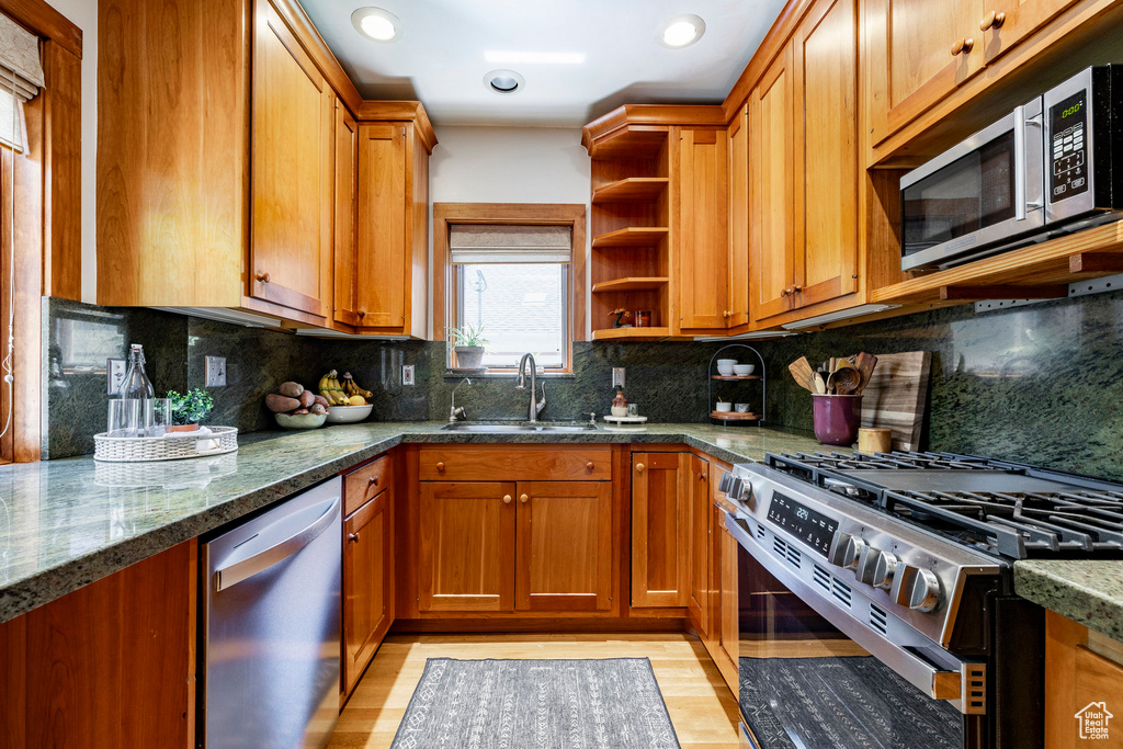 Kitchen with stainless steel appliances, open shelves, brown cabinetry, dark stone counters, and recessed lighting