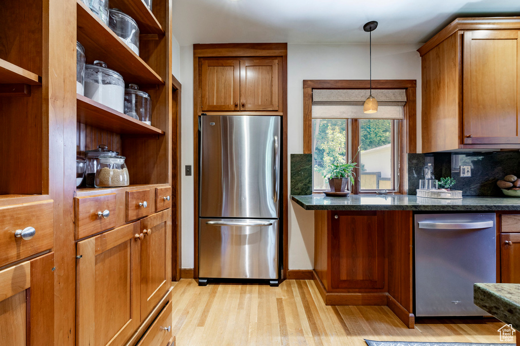 Kitchen with stainless steel appliances, light wood-style flooring, tasteful backsplash, and brown cabinets