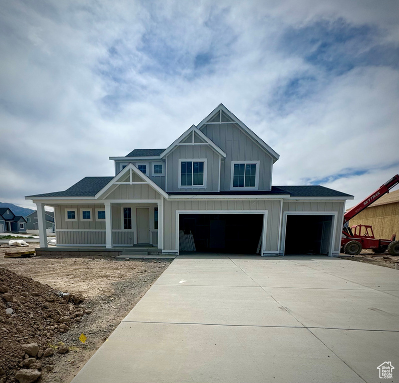 View of front of home with a porch, driveway, board and batten siding, an attached garage, and roof with shingles