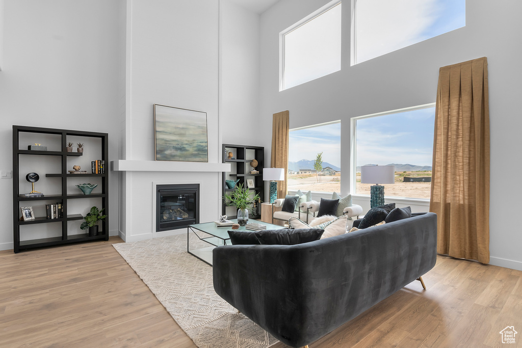 Living room with a high ceiling, wood finished floors, a glass covered fireplace, and baseboards
