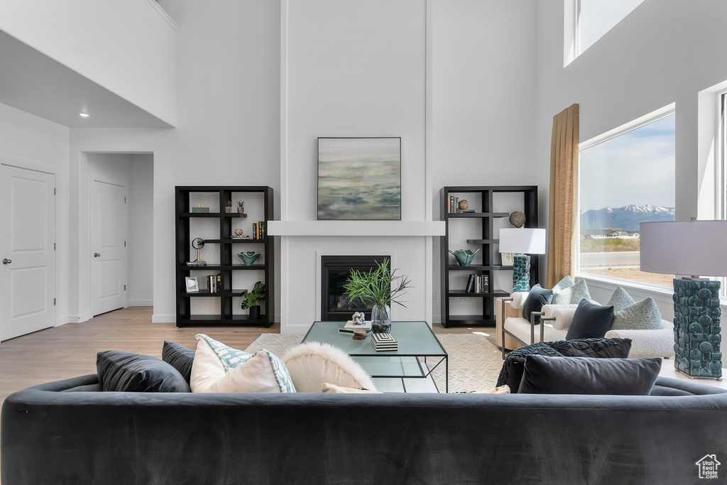 Living area featuring a high ceiling, plenty of natural light, a glass covered fireplace, and wood finished floors