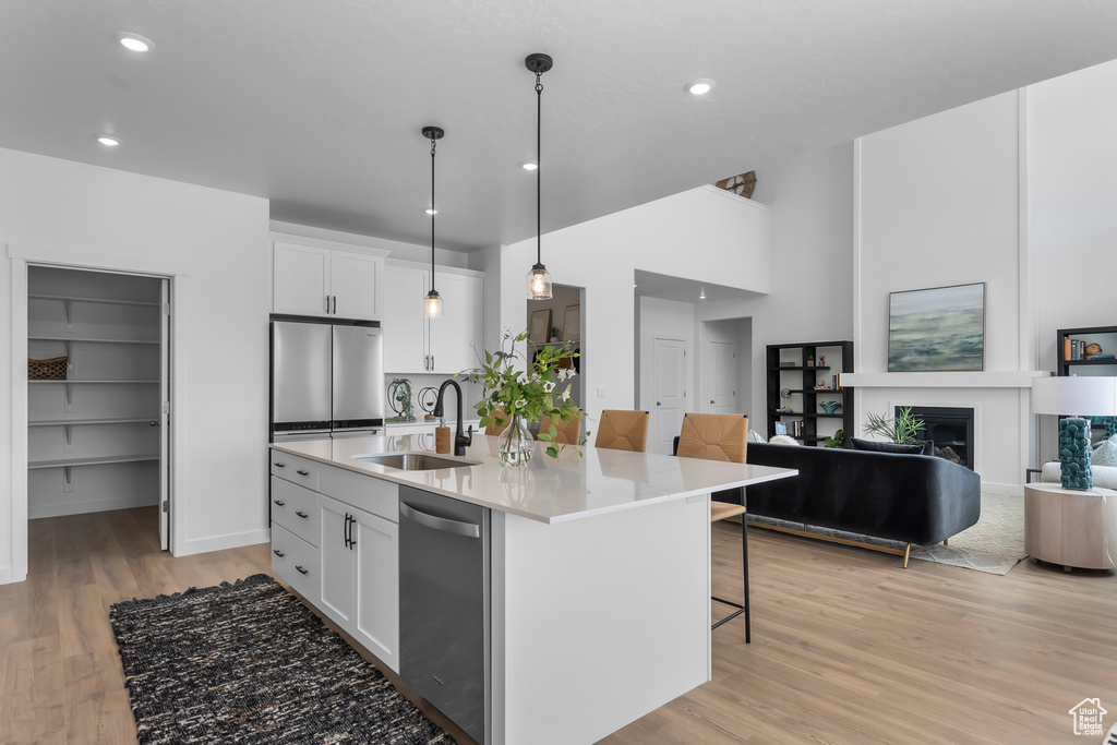 Kitchen featuring stainless steel appliances, a sink, light wood-type flooring, white cabinets, and a breakfast bar