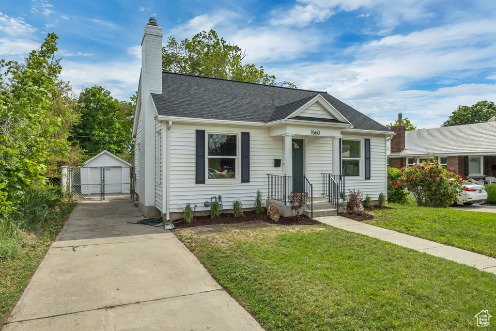 Bungalow-style home with an outdoor structure, a front yard, a chimney, a garage, and roof with shingles