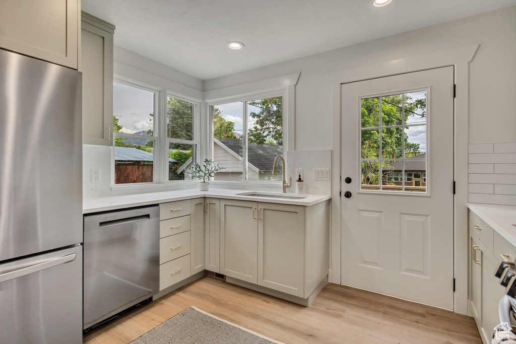 Kitchen with stainless steel appliances, a sink, light wood-style flooring, light countertops, and recessed lighting
