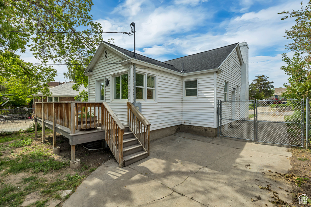 Rear view of property with a deck, roof with shingles, a gate, and a chimney