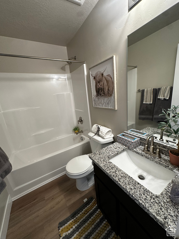 Bathroom featuring wood finished floors, washtub / shower combination, vanity, toilet, and a textured ceiling
