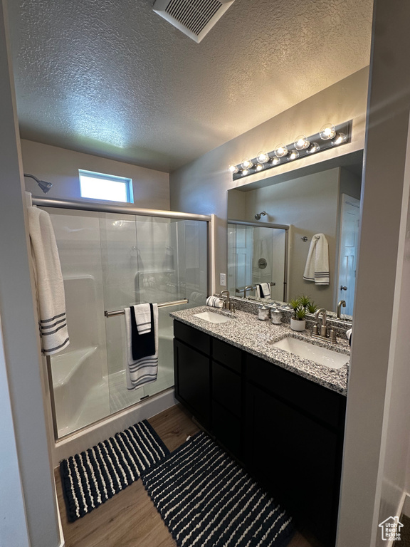 Full bathroom with wood finished floors, a shower stall, double vanity, and a textured ceiling