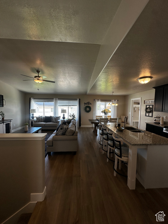 Living room with a textured ceiling, dark wood-style flooring, a ceiling fan, a chandelier, and baseboards