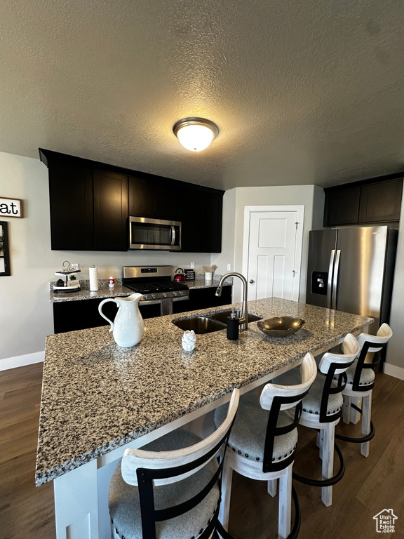 Kitchen featuring stainless steel appliances, a sink, baseboards, stone counters, and a textured ceiling