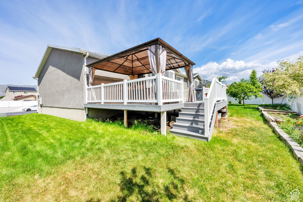 Back of property with a gazebo, a lawn, a deck, and stucco siding