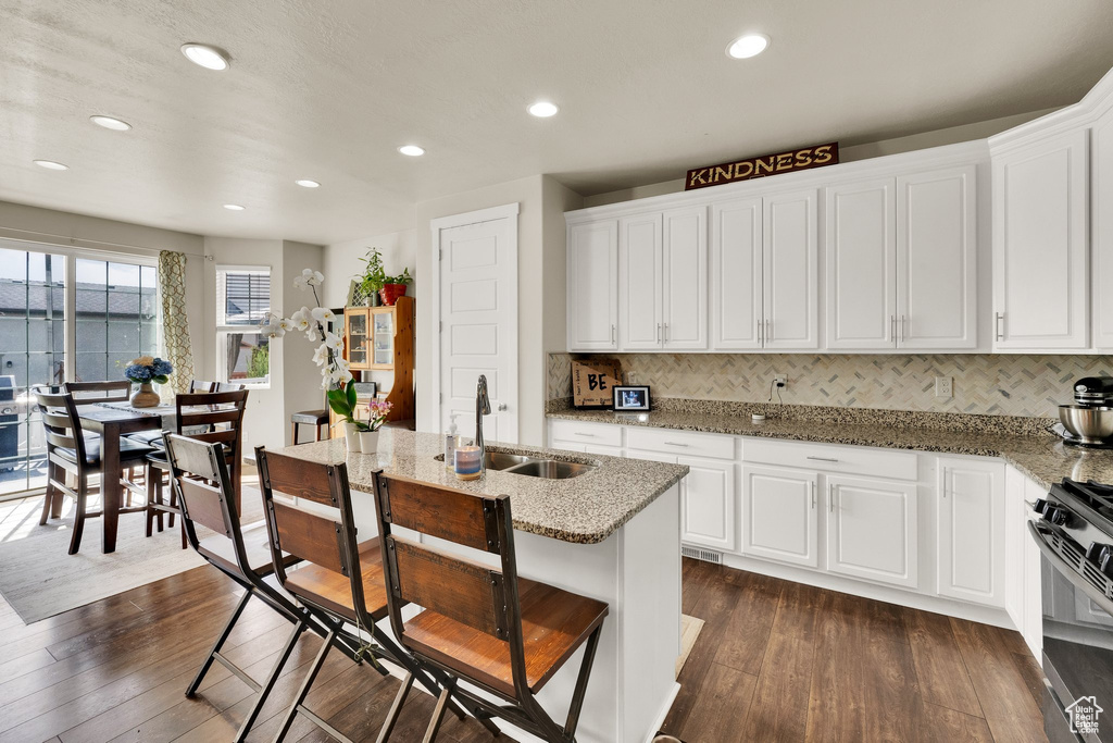 Kitchen with dark wood-style floors, stainless steel range with gas stovetop, recessed lighting, light stone countertops, and white cabinets