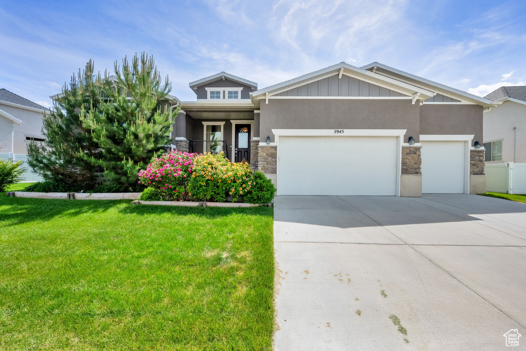 View of front of home with stone siding, a front yard, an attached garage, concrete driveway, and stucco siding