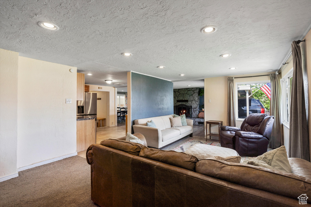 Living room with a textured ceiling, light carpet, recessed lighting, a stone fireplace, and baseboards
