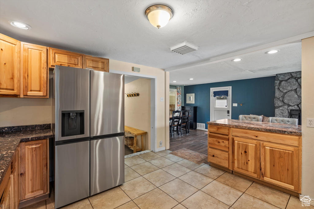 Kitchen featuring stainless steel fridge with ice dispenser, dark countertops, light tile patterned flooring, and recessed lighting