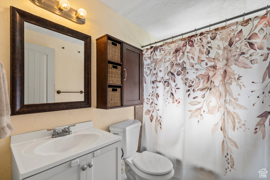 Full bath with vanity, toilet, a textured wall, curtained shower, and a textured ceiling