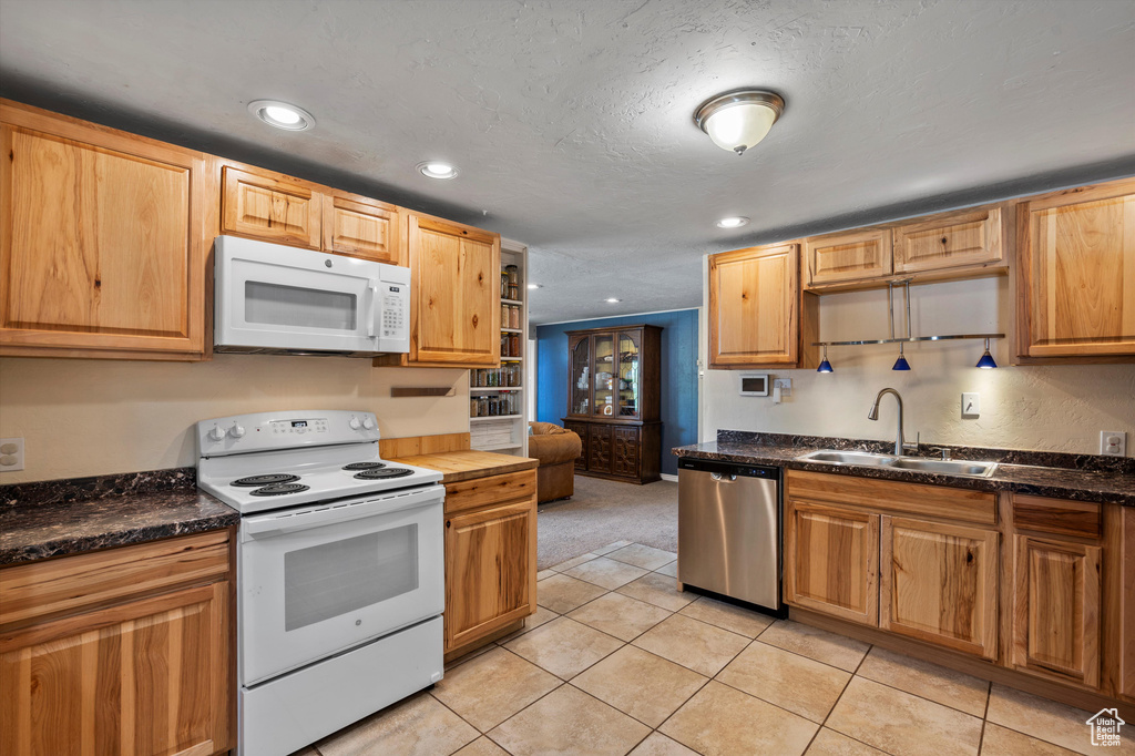 Kitchen with white appliances, a sink, recessed lighting, light tile patterned floors, and light colored carpet