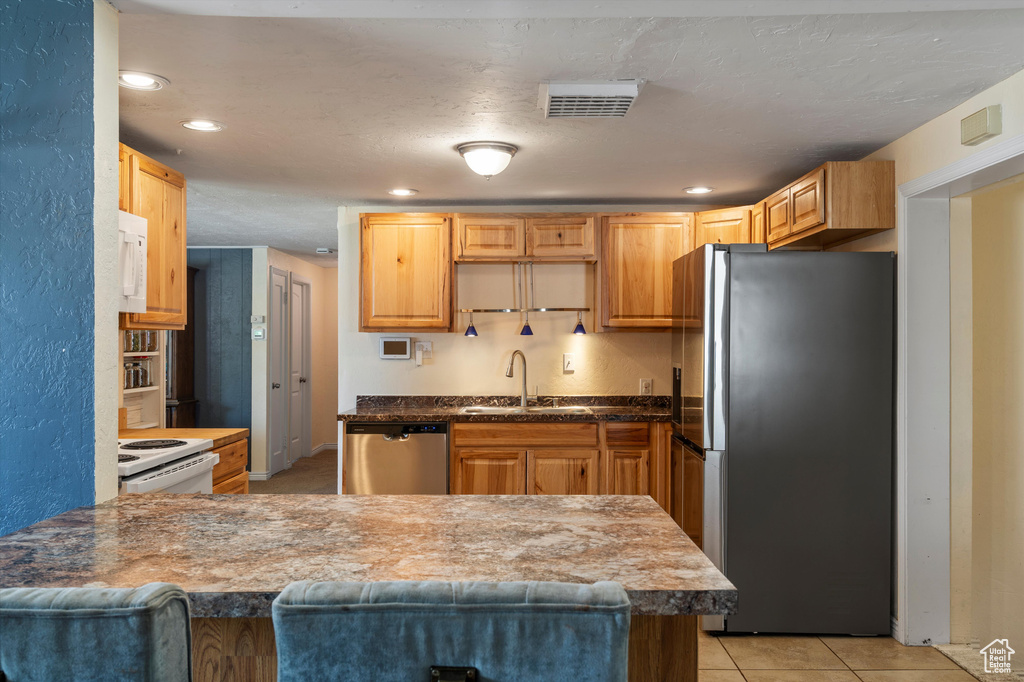 Kitchen with appliances with stainless steel finishes, a sink, a peninsula, light tile patterned floors, and recessed lighting