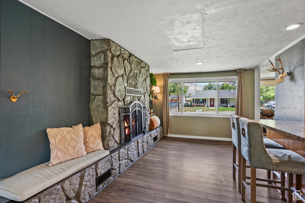 Living area featuring a stone fireplace, wood finished floors, baseboards, and a textured ceiling