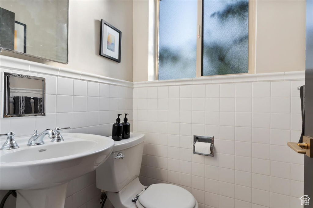 Half bathroom featuring tile walls, toilet, and a sink