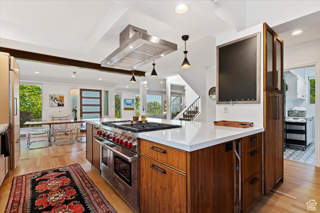 Kitchen with premium appliances, wall chimney range hood, light wood-type flooring, light countertops, and decorative light fixtures