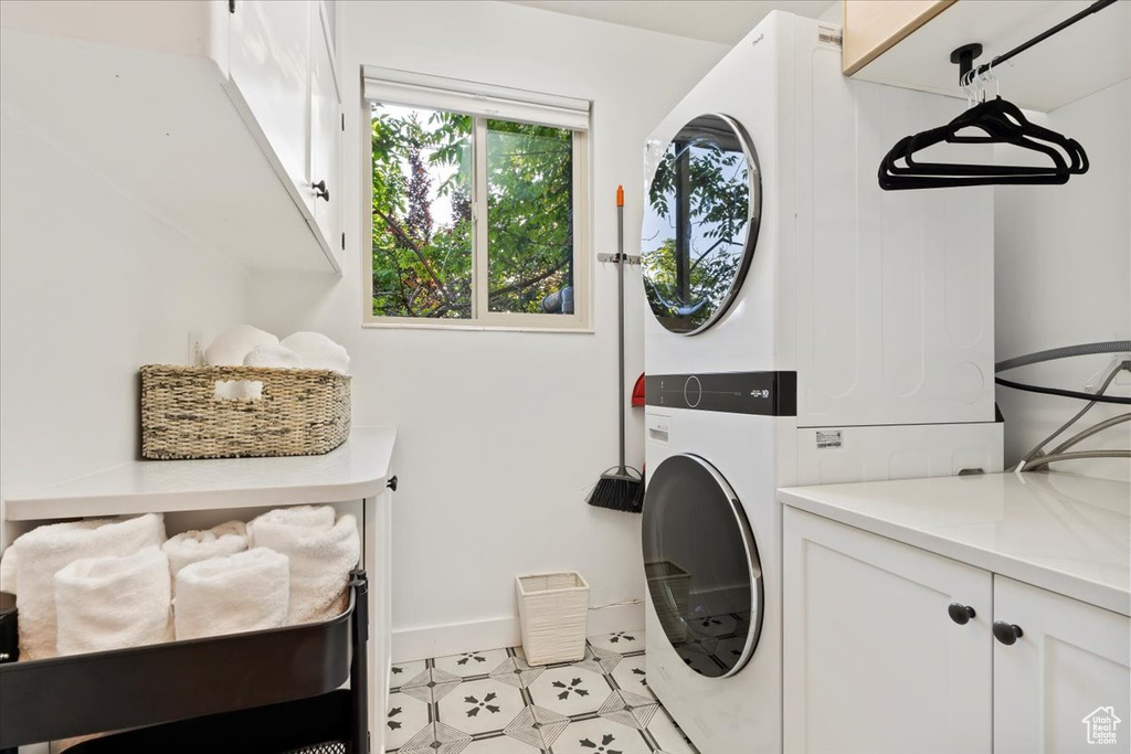 Laundry area with cabinet space, stacked washer / drying machine, baseboards, and light tile patterned flooring