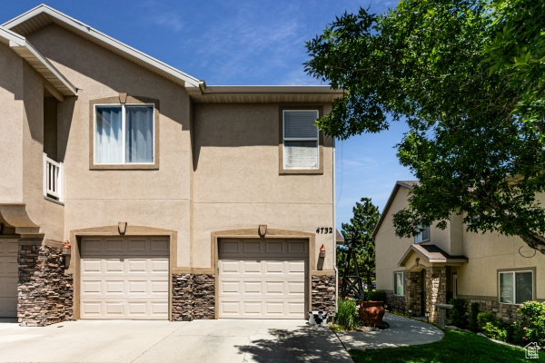 Townhome / multi-family property with stone siding, concrete driveway, a garage, and stucco siding