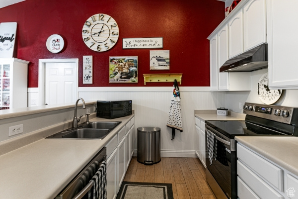 Kitchen featuring appliances with stainless steel finishes, under cabinet range hood, a sink, white cabinetry, and light wood-style floors