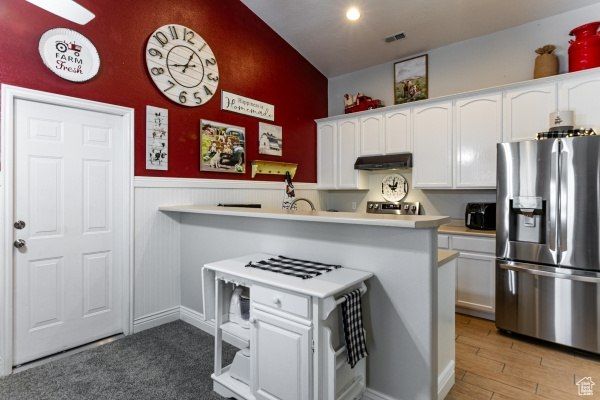 Kitchen featuring stainless steel refrigerator with ice dispenser, under cabinet range hood, white cabinetry, light countertops, and wainscoting