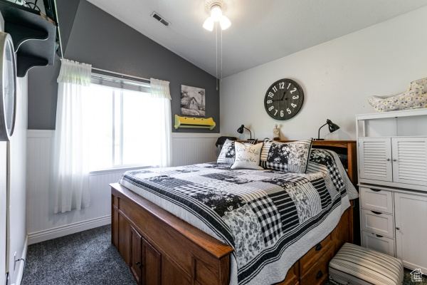 Bedroom featuring lofted ceiling, dark carpet, wainscoting, and refrigerator