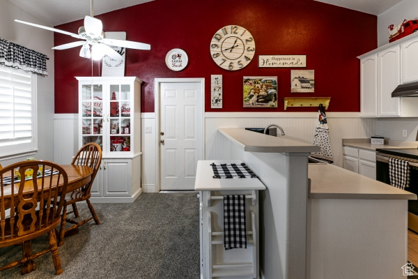 Kitchen featuring vaulted ceiling, ceiling fan, a wainscoted wall, white cabinets, and range