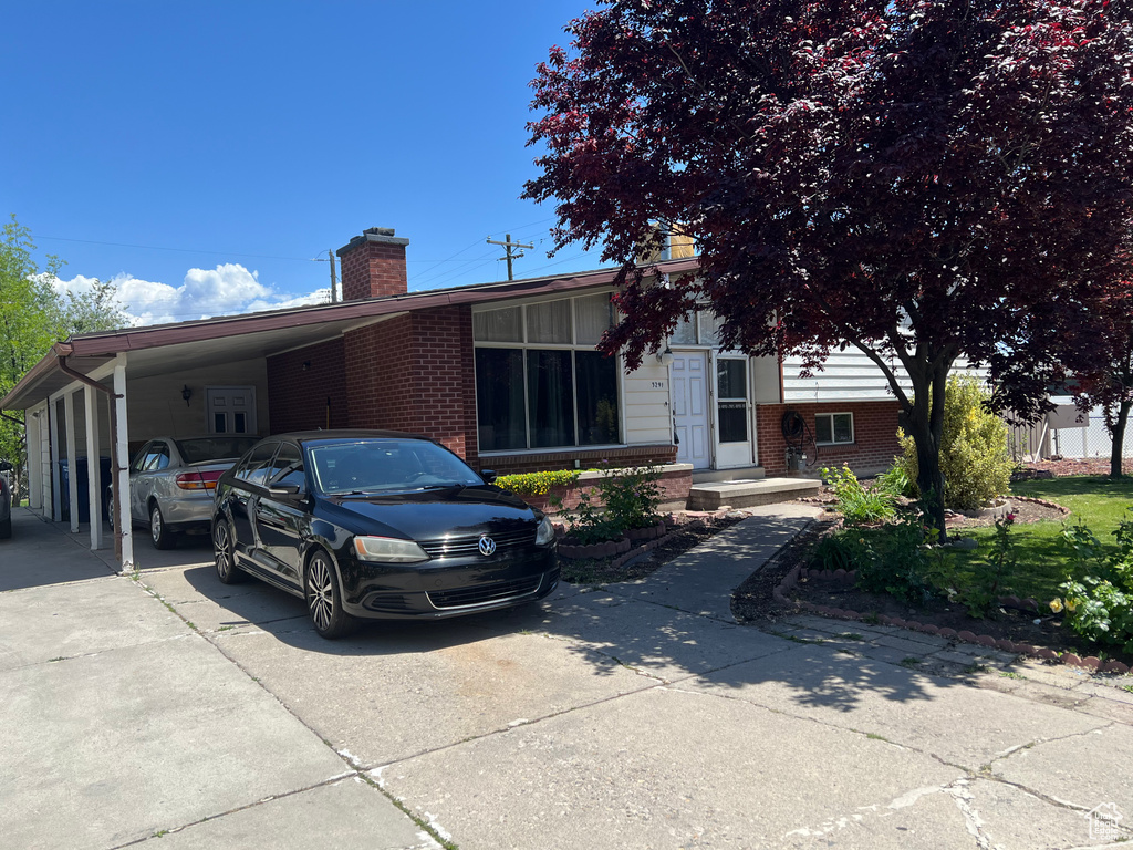 View of front of property with a chimney, a carport, brick siding, and driveway